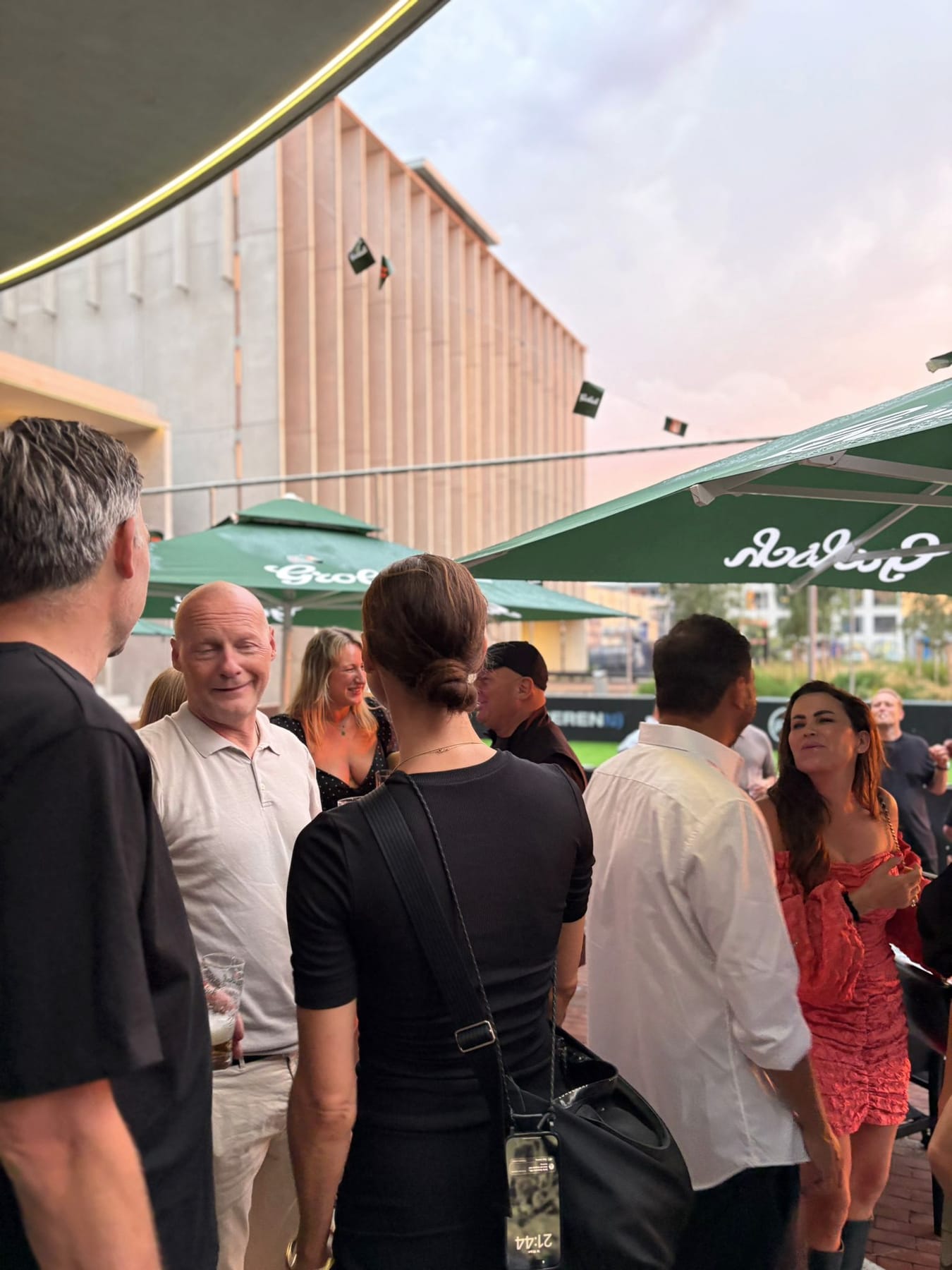 Gasten borrelen bij zonsondergang op het plein voor The Scene, onder de parasols
