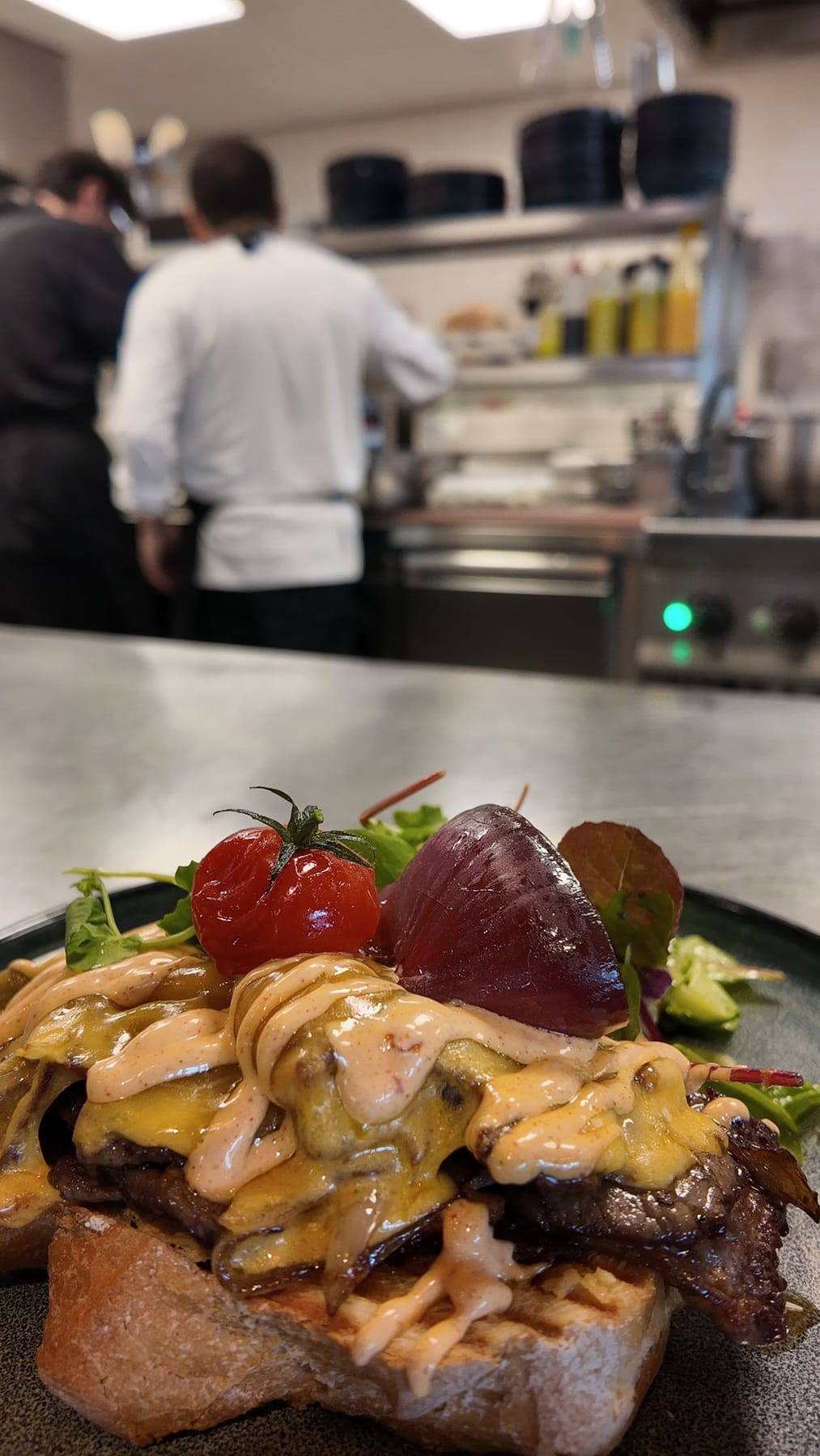 Twee koks aan de pass in de keuken van The Scene, met een bord Broadway Beef op de voorgrond
